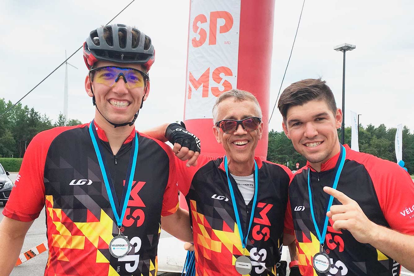 Trois cyclistes en maillot rouge et noir, médaille au cou, après une course