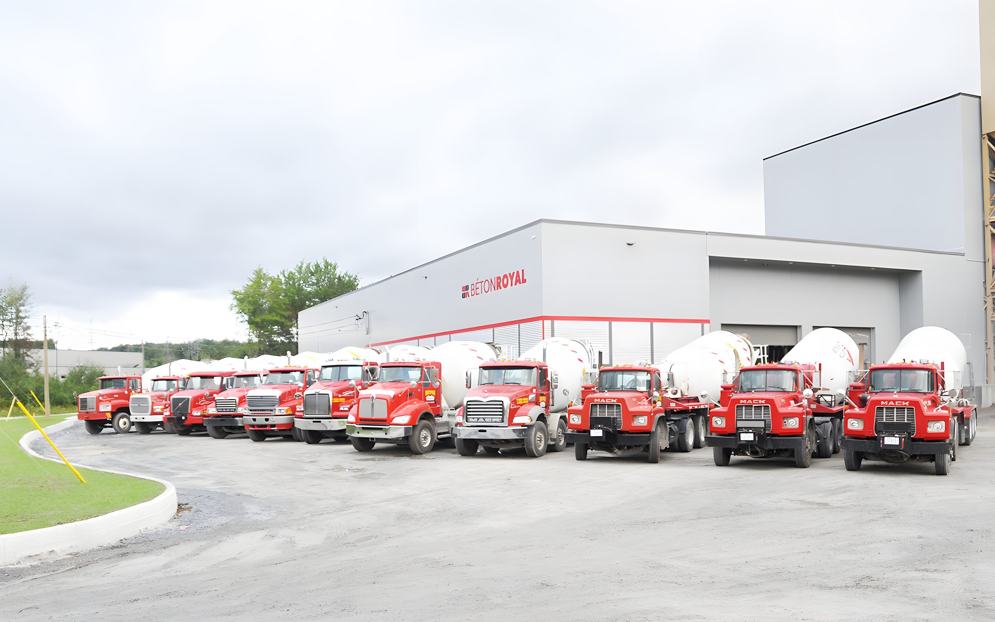 Une dizaine de bétonnières rouges alignées devant l'usine Béton Royal, le silo derrière